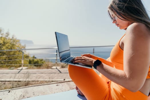 Digital nomad, Business woman working on laptop by the sea. Pretty lady typing on computer by the sea at sunset, makes a business transaction online from a distance. Freelance, remote work on vacation