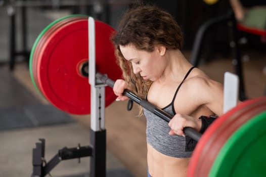 Middle-aged woman doing squats with a barbell in the gym