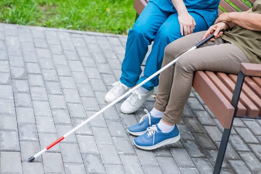 A nurse and an elderly blind woman are sitting on a bench in the park. Close up of legs