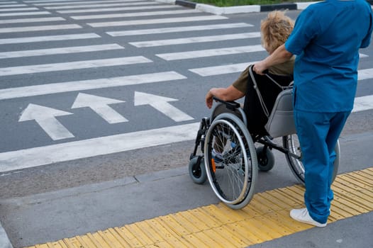 Rear view of a nurse helping an elderly woman in a wheelchair cross the road