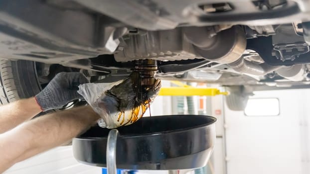 A mechanic drains a car's used engine oil