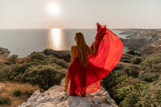 Woman sunset sea red dress, back view a happy beautiful sensual woman in a red long dress posing on a rock high above the sea on sunset