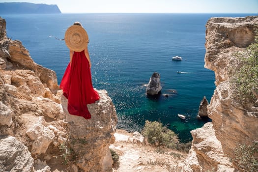 woman in a red dress stands on a cliff overlooking the ocean. The scene is serene and peaceful, with the woman's hat and dress adding a touch of elegance to the image