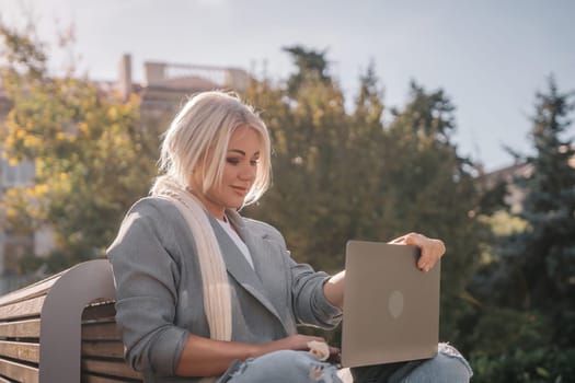 A woman is sitting on a bench with a laptop in front of her. She is smiling and she is enjoying her time