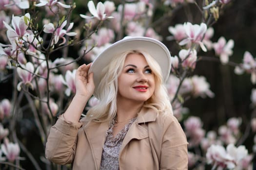 Magnolia flowers woman. A blonde woman wearing a white hat stands in front of a tree with pink flowers. She has a smile on her face and she is enjoying the beautiful scenery