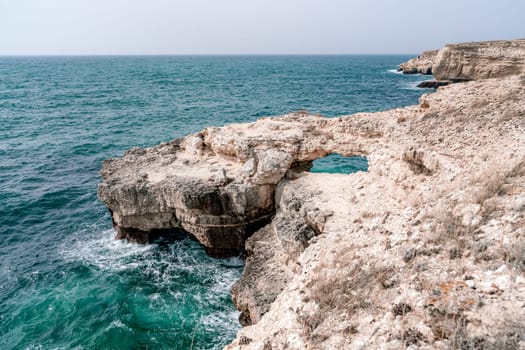 A rocky cliff overlooks the ocean. The water is calm and the sky is clear. The scene is peaceful and serene