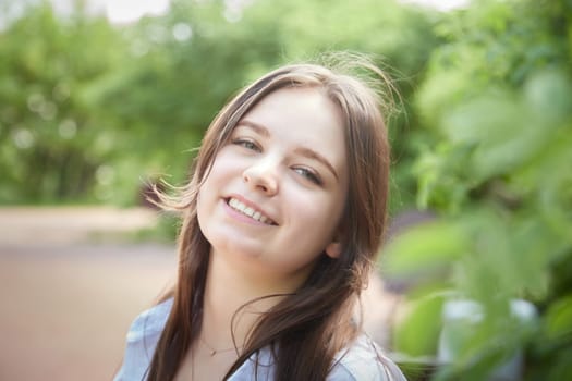 Portrait of a happy girl in the park in summer. Holidays, rest, youth. A young girl with curly hair in a green park on a summer day