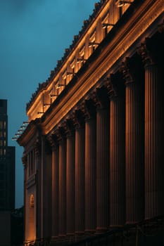 The majestic architecture of a historical building is illuminated during dusk with a cityscape in the background