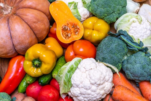 Various vegetables are laid out on a wooden table. Large assortment of vegetables food. pumpkin cabbage broccoli pepper tomatoes carrots and others.