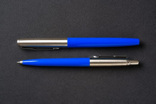 Blue plastic and metal ballpoint pen and fountain pen on dark gray isolated background