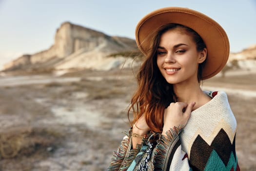 Serene woman in stylish hat and cozy sweater standing in desert landscape with mountains afar