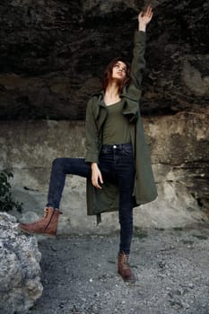 Woman in green coat standing triumphantly on rock with arms raised high