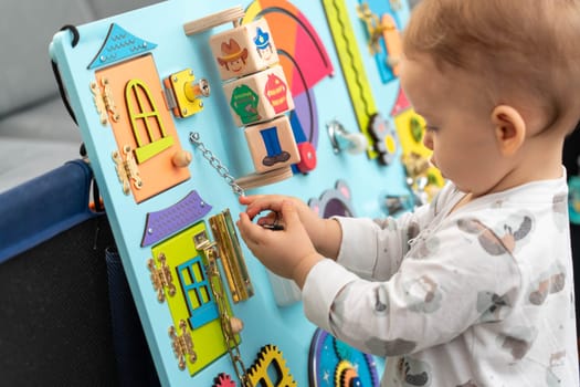 Baby holding a key on a chain while playing with a busy board.