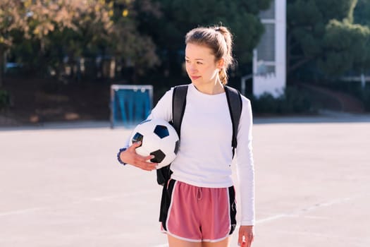 young caucasian woman walking at urban football court with a soccer ball in hand, concept of sport and active lifestyle