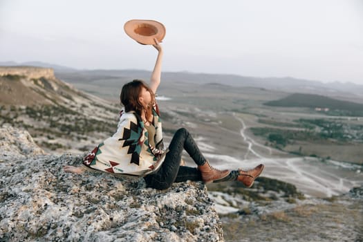 Woman triumphantly throwing her hat in the air while sitting on a mountain summit