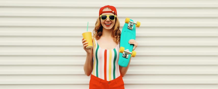 Summer portrait of happy cheerful stylish young woman with skateboard and cup of fresh juice in colorful clothes posing on white background