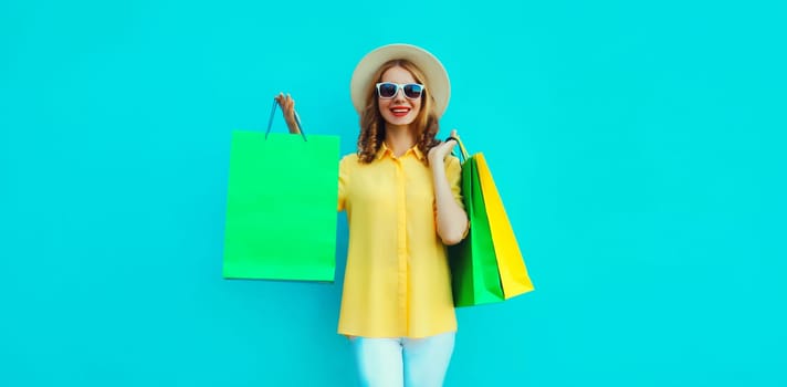 Stylish beautiful happy smiling young woman posing with bright colorful shopping bags wearing summer straw hat on blue background