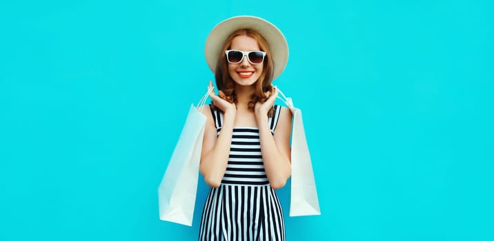 Stylish beautiful happy smiling young woman posing with white shopping bags wearing summer straw hat on blue background