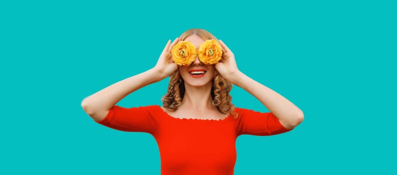 Summer portrait of beautiful happy smiling woman covering her eyes with flower buds as binoculars looking for something on blue studio background