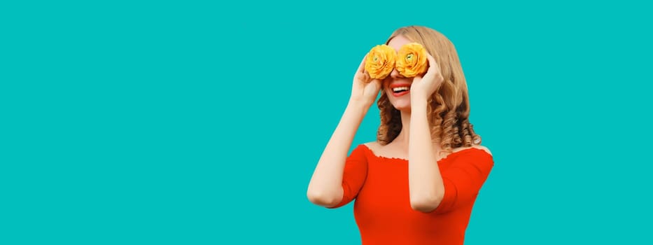 Summer portrait of beautiful happy smiling woman covering her eyes with flower buds as binoculars looking for something on blue studio background