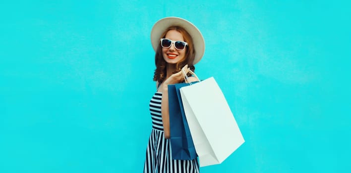 Stylish beautiful happy smiling young woman posing with white shopping bags wearing summer straw hat on blue background