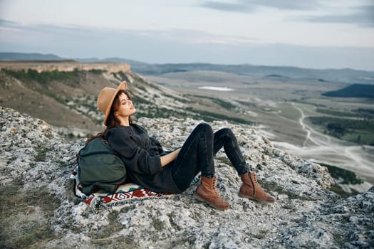 Serene hiker enjoying breathtaking view from mountain summit with backpack and hat resting on rock