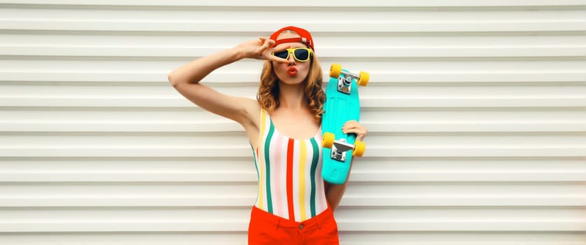 Summer portrait of modern cheerful stylish young woman with skateboard in colorful clothes posing on white background