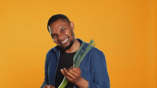 Happy person having fun playing guitar at a leek in studio, acting funny and mimicking a green onion as a musical instrument. Young guy being silly with organic vegetables. Camera A.
