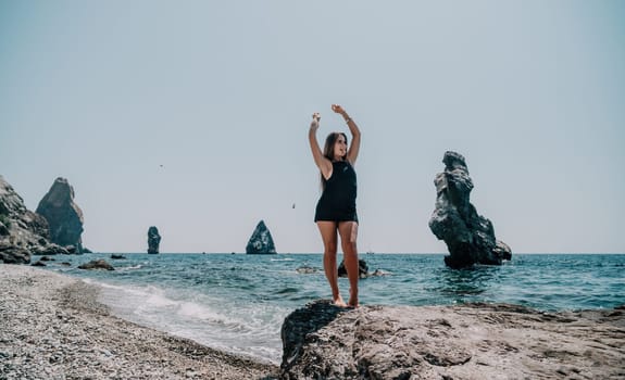 Woman travel sea. Young Happy woman in a long red dress posing on a beach near the sea on background of volcanic rocks, like in Iceland, sharing travel adventure journey