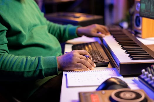 In his home studio, songwriter writes down lines and melodic elements to create new tunes. Using digital audio workstation software, composing and recording songs in post production.