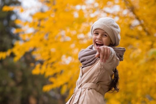 Happy caucasian girl in a beige coat and beret walks in the park in autumn