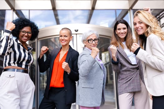 Five multiethnic women in happy formal wear with happy fists up looking at camera