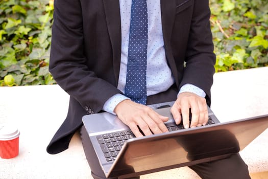 Business on the move: Businessman working on his laptop on the street. Man Hands Type On His Laptop Outdoors