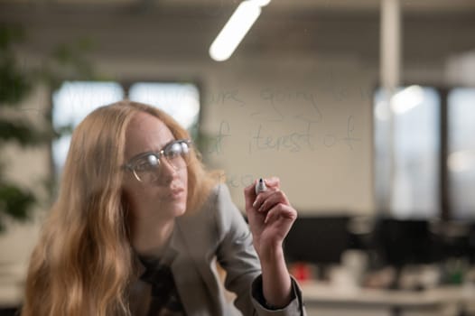 Caucasian woman with glasses writes text in English on a glass wall