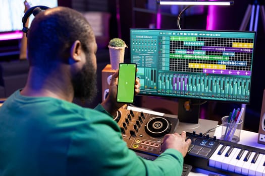 Male technician using mixing console and piano to edit tunes, having isolated mockup screen. Composer producing new music with mixing and mastering techniques in his home studio.