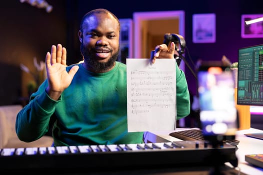 Talented composer explaining musical sheet notes during an online master class recorded with smartphone in home studio. Artist musician teaching people how to read and sing the accords on piano.