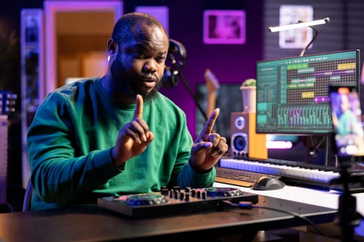 Young producer teaching people to use a mixing console during online lessons, recording himself with a smartphone. Sound engineer hosting a master class to teach editing in post production.