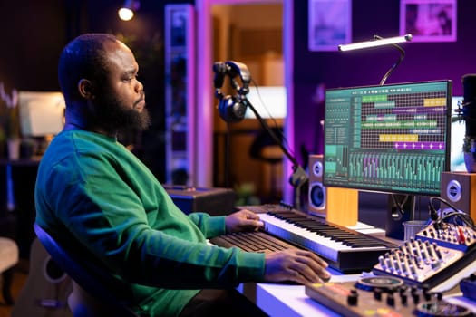 African american artist composing a new soundtrack for a project, using professional production software in his home studio. Skilled creative singer producing music and adding sound effects.