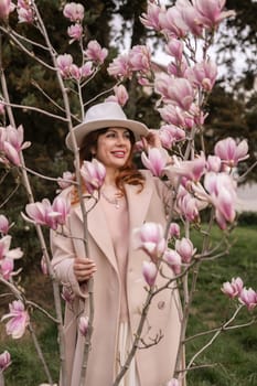 Woman magnolia flowers, surrounded by blossoming trees, hair down, white hat, wearing a light coat. Captured during spring, showcasing natural beauty and seasonal change