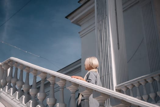 A woman is standing on a white staircase with a cup in her hand. She is smiling and looking up at the sky