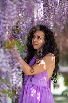 Woman wisteria lilac dress. Thoughtful happy mature woman in purple dress surrounded by chinese wisteria.