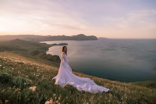 A woman in a white dress stands on a hill overlooking the ocean. The scene is serene and peaceful, with the woman's dress flowing in the wind