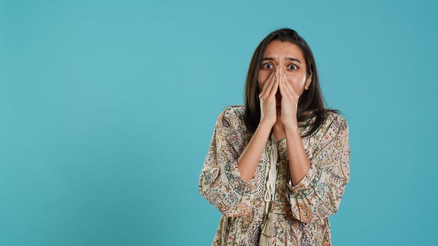 Anxious indian woman covering face with palms, worried about future, isolated over studio background. Tense person shocked by troubling news, gasping, feeling distressed, camera A