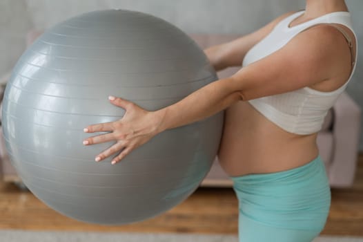 Pregnant red-haired woman doing arm exercises with fitball at home