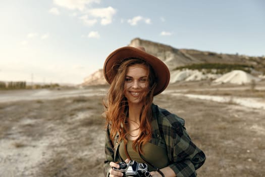 Woman in plaid shirt and hat capturing scenic mountain view with camera in field