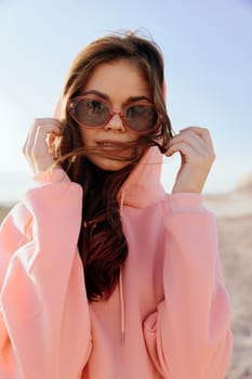 Relaxing day at the beach woman in pink hoodie and sunglasses with hands on head by the water