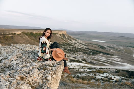 Adventure awaits woman in hat sits on rock in front of majestic mountain range