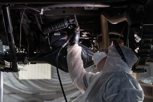 The master sprays an anti-corrosion compound on the bottom of the car