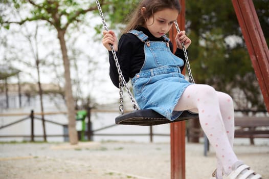 Cute child girl looking sad, swinging on the outdoors playground. People. Childhood concept. Lifestyle