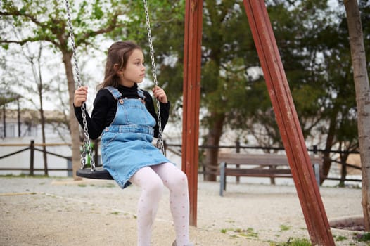 Cute child girl swinging on the outdoors playground. People. Happy carefree childhood concept. Lifestyle